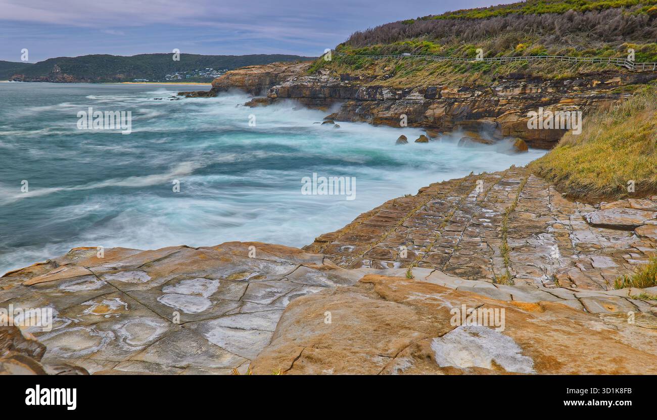 Longue exposition des vagues sauvages de l'océan le long de falaise et de la côte rocheuse avec pavement pavé caractéristique dans le parc national de Bouddi, Nouvelle-Galles du Sud, Australie Banque D'Images