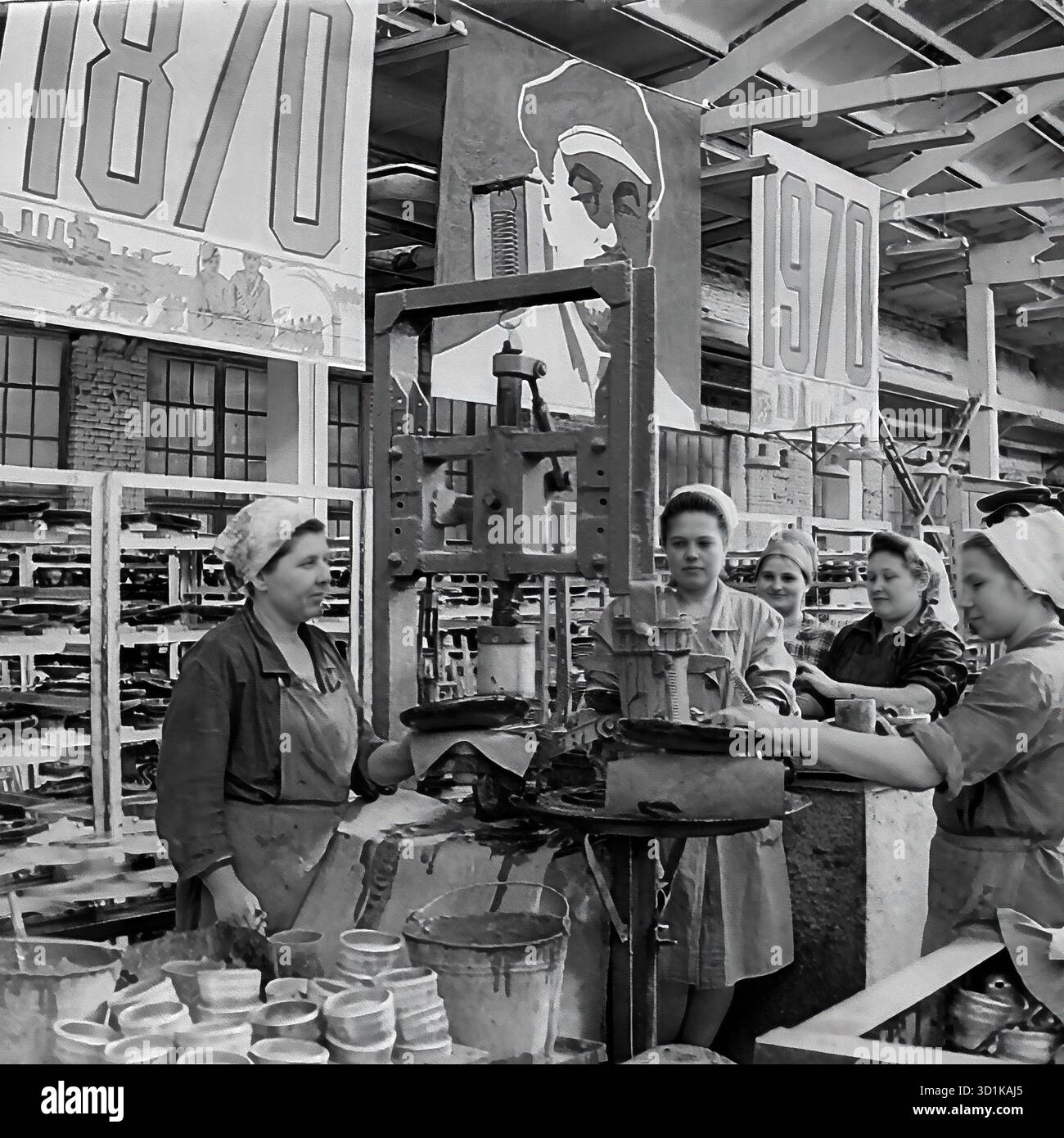URSS, RSS d'Ukraine, Sloviansk, oblast de Donetsk. 1970. Atelier de blindage à l'usine d'armature et d'isolation de Sloviansk (AIZ). Un groupe de travailleuses (une brigade) à leur poste de travail par une presse, utilisée pour assembler des isolateurs haute tension. L'ensemble de l'atelier est lourdement décoré pour une célébration d'état. D'énormes bannières avec les dates '1870' et '1970' et un grand portrait de Vladimir Lénine pendent au plafond, marquant le 100ème anniversaire (centenaire) de sa naissance. Cette photo d'archives en noir et blanc capture la vie industrielle soviétique et la propagande d'État. Banque D'Images