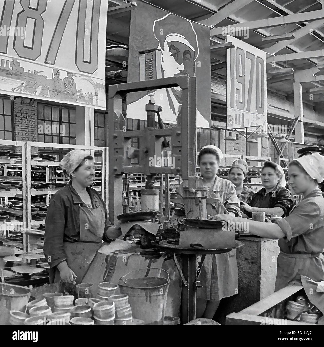 URSS, RSS d'Ukraine, Sloviansk, oblast de Donetsk. 1970. Atelier de blindage à l'usine d'armature et d'isolation de Sloviansk (AIZ). Un groupe de travailleuses (une brigade) à leur poste de travail par une presse, utilisée pour assembler des isolateurs haute tension. L'ensemble de l'atelier est lourdement décoré pour une célébration d'état. D'énormes bannières avec les dates '1870' et '1970' et un grand portrait de Vladimir Lénine pendent au plafond, marquant le 100ème anniversaire (centenaire) de sa naissance. Cette photo d'archives en noir et blanc capture la vie industrielle soviétique et la propagande d'État. Banque D'Images