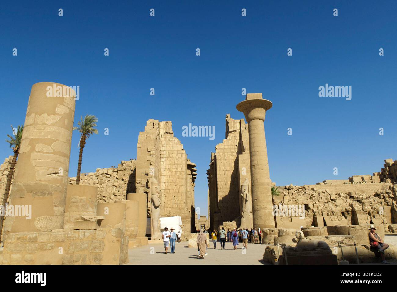 Les touristes explorent des ruines antiques avec des colonnes imposantes et des murs de pierre en ruine sous un ciel bleu clair au complexe du temple de Karnak près de Louxor, en Égypte Banque D'Images