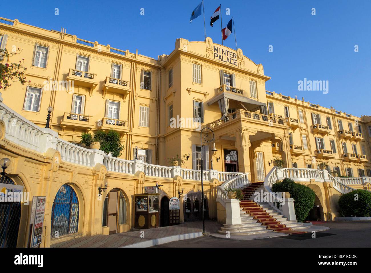 Façade jaune historique de l'Hôtel Winter Palace avec drapeaux volants et escalier courbé sous un ciel bleu clair Banque D'Images