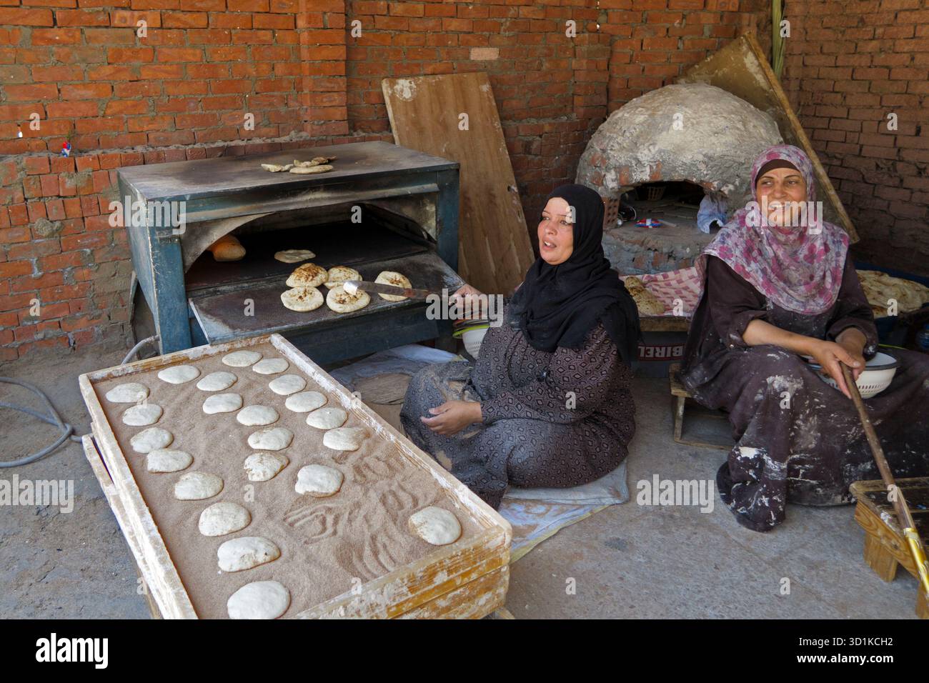 Deux femmes cuisant du pain plat traditionnel dans un cadre rustique de murs de briques en utilisant des fours en argile et en métal en Égypte Banque D'Images