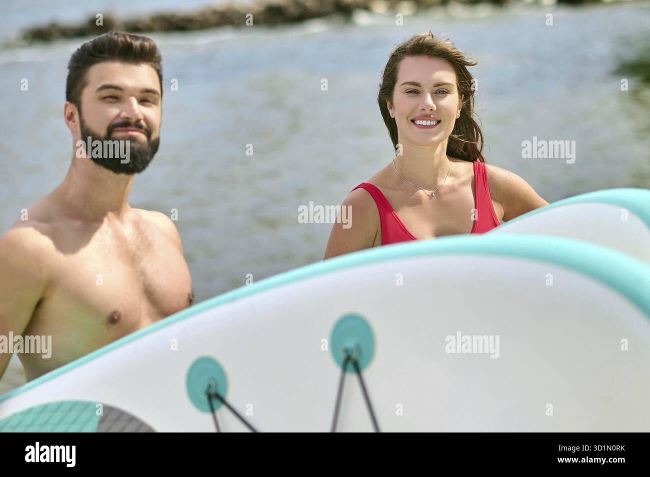 Attrayant homme et femme jeunes surfeurs sur la plage, profitant de vacances près de la mer et du sport extrême, exprimant des émotions positives Banque D'Images