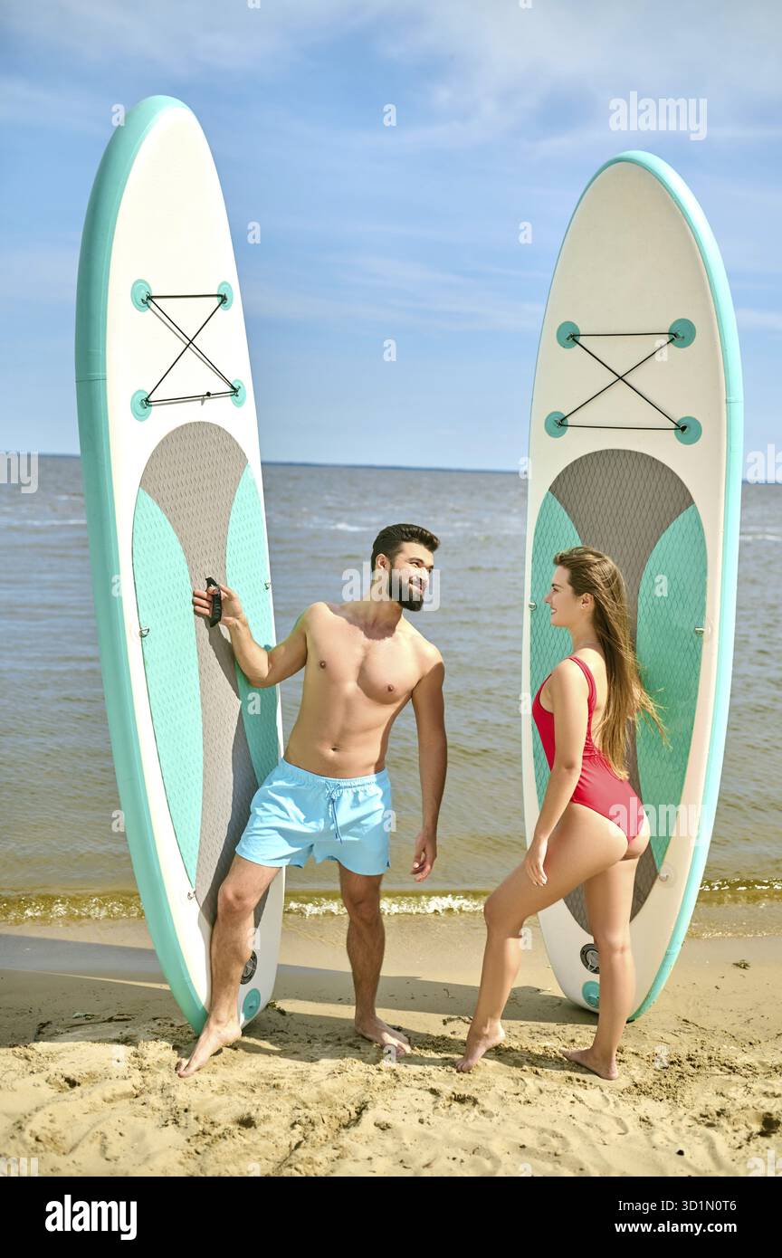 Attrayant homme et femme jeunes surfeurs sur la plage, profitant de vacances près de la mer et du sport extrême, exprimant des émotions positives Banque D'Images