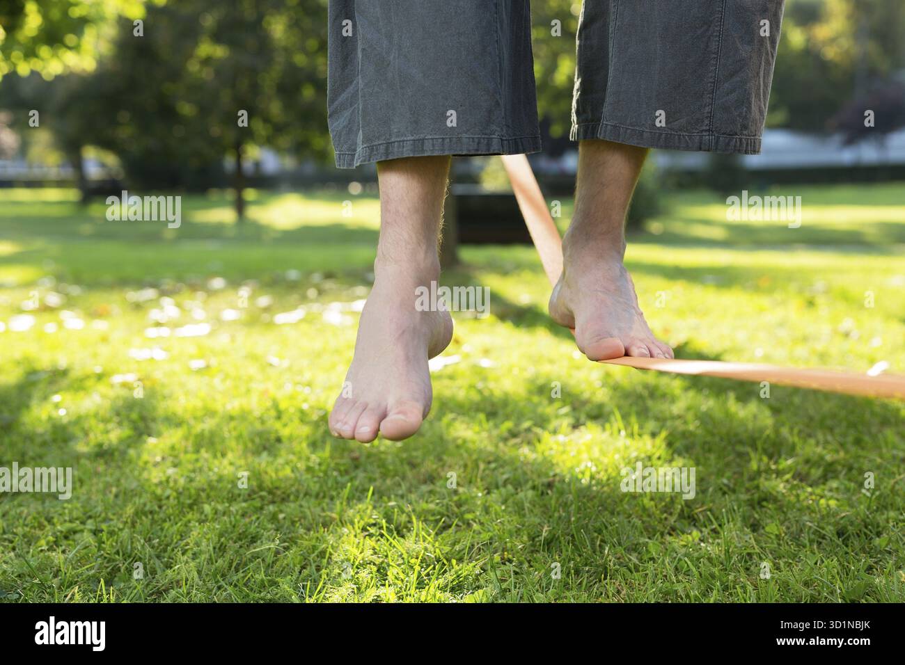 Gros plan des pieds d'homme équilibrant une corde serrée ou slackline dans un environnement de parc avec un pied au-dessus de la corde Banque D'Images