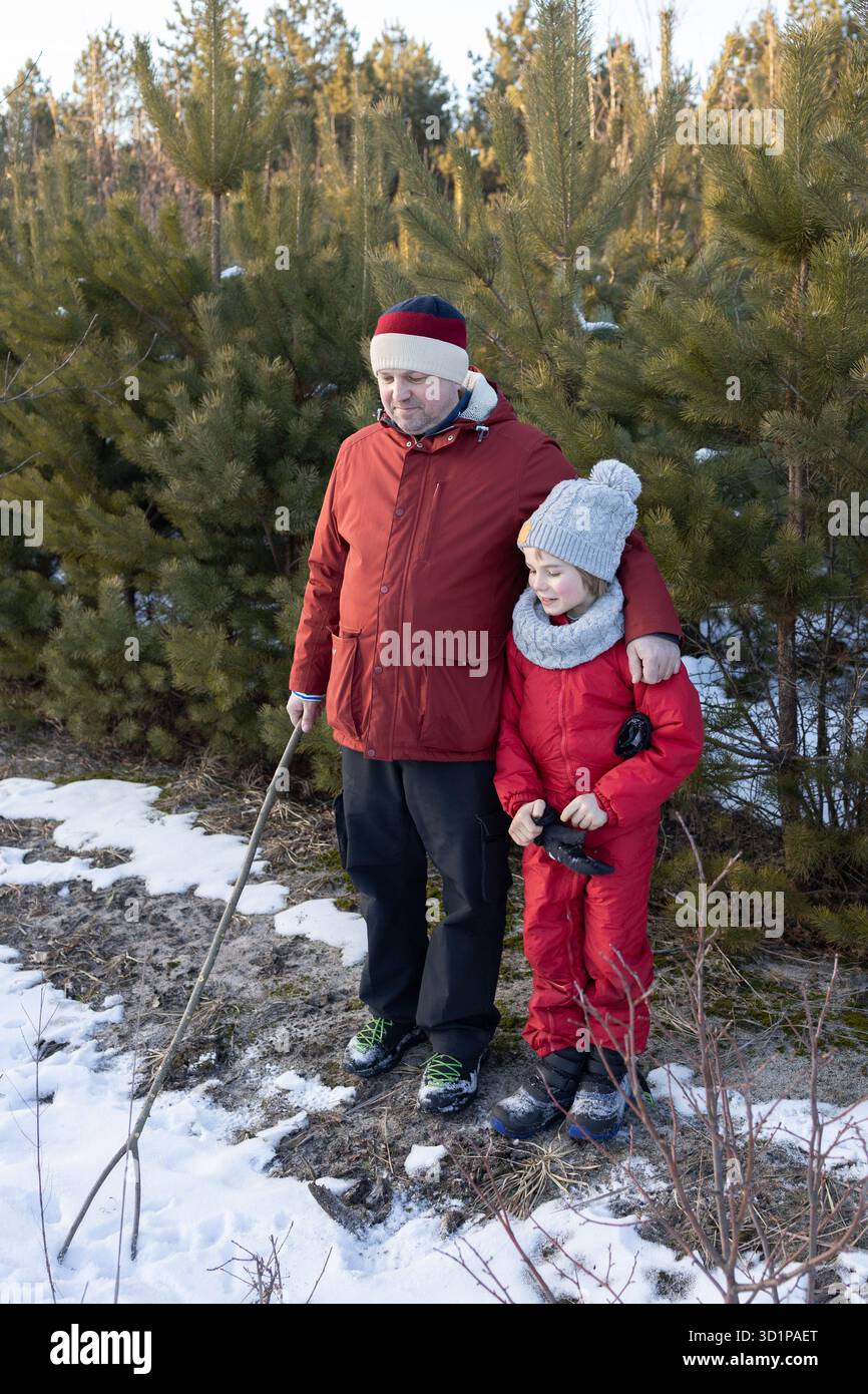Papa et fils en vêtements chauds se promenant dans un parc enneigé en hiver. Mode de vie actif, promenades familiales dans la nature. Banque D'Images