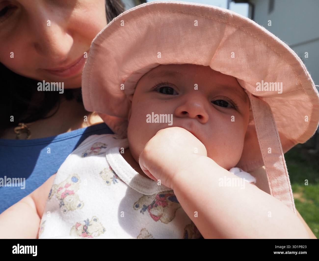 Mère tenant doucement bébé dans un chapeau rose, gros plan portrait montrant l'amour et la tendresse. Lumière chaude et connexion familiale. Banque D'Images