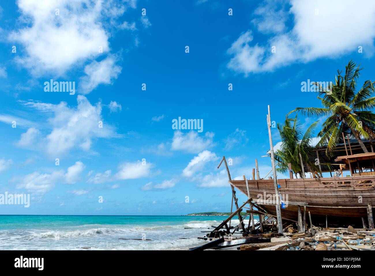 Bateau traditionnel en bois en construction sur la plage tropicale avec des palmiers, ciel bleu clair et mer turquoise dans un cadre côtier éloigné Banque D'Images
