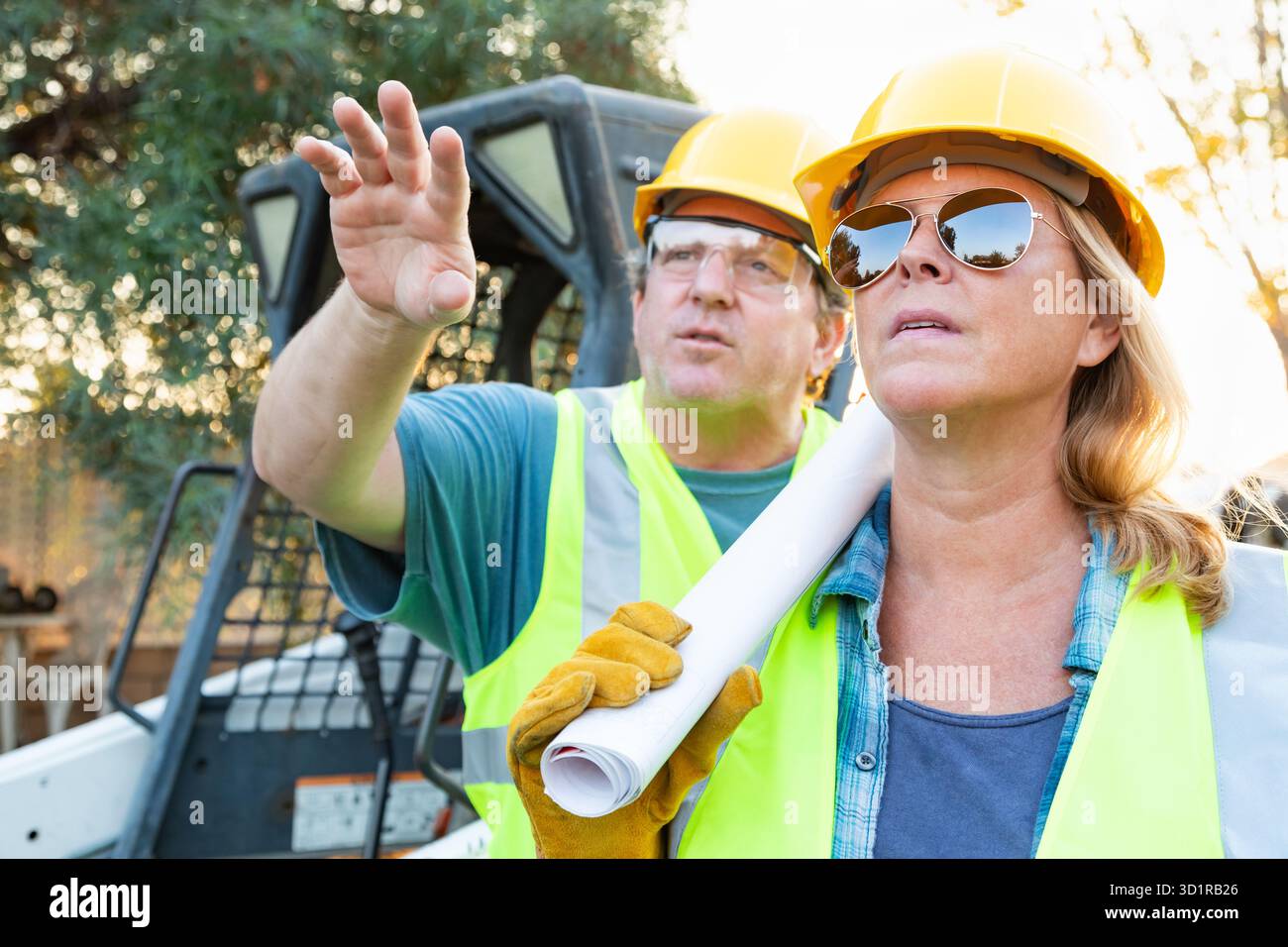 Les travailleurs hommes et femmes avec des modèles techniques Talking at Construction Site Banque D'Images