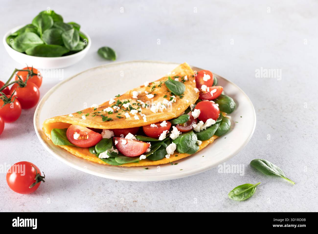Omelette farcie avec tomates, fromage et épinards sur fond blanc. Banque D'Images