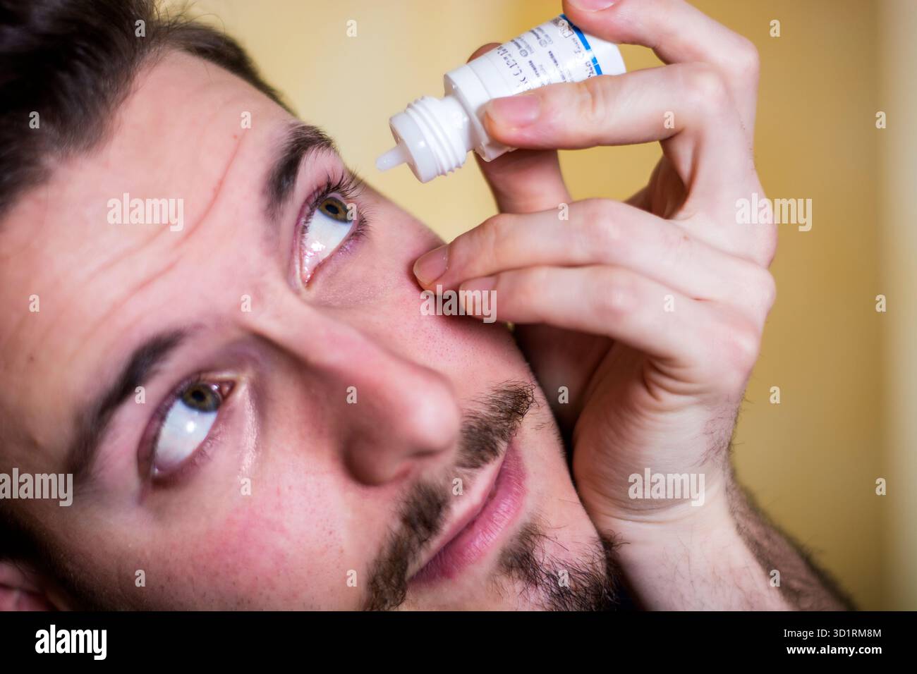 Beau jeune homme qui laisse tomber des médicaments dans l'oeil Banque D'Images
