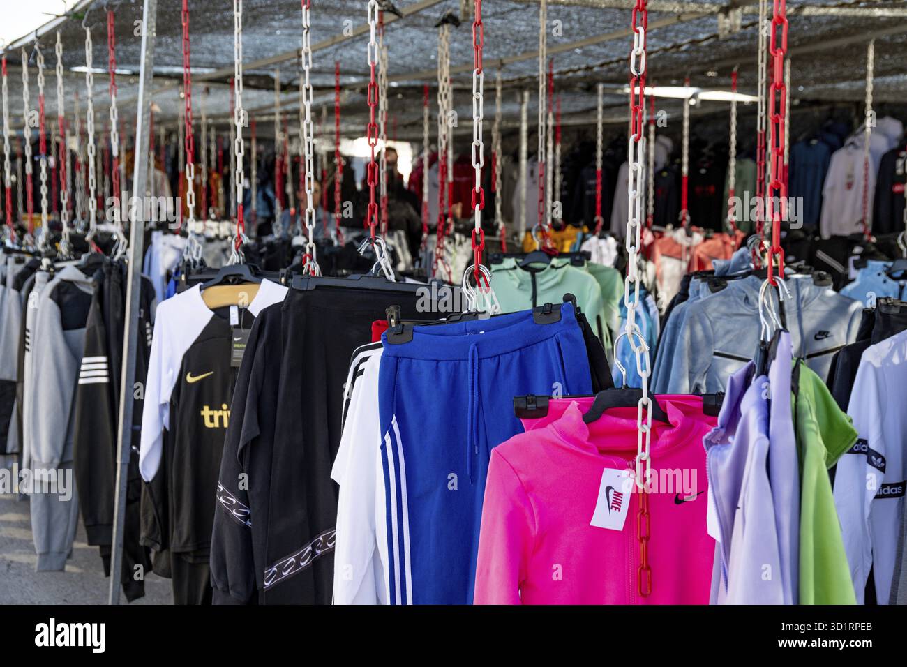 Guadix, Grenade - Espagne - 2024 : stand de marché présentant des vêtements de sport suspendus à des chaînes rouges et blanches, des vestes colorées et des pantalons avec BR visible Banque D'Images