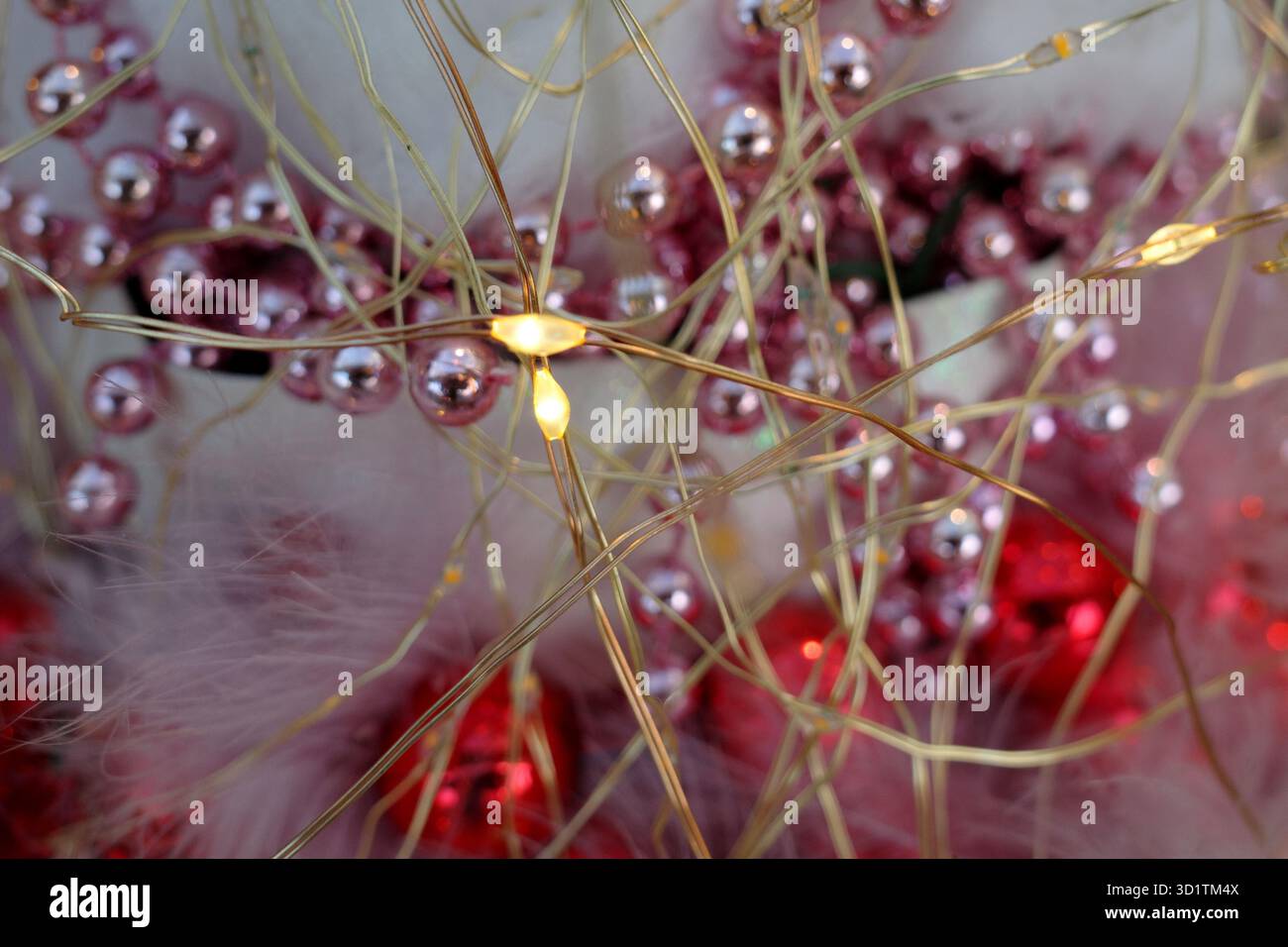 Les lumières LED jaunes avec un mince fil doré forment un affichage décoratif. Autour des lumières se trouvent de petites guirlandes de perles roses brillantes avec une boule rouge floue Banque D'Images