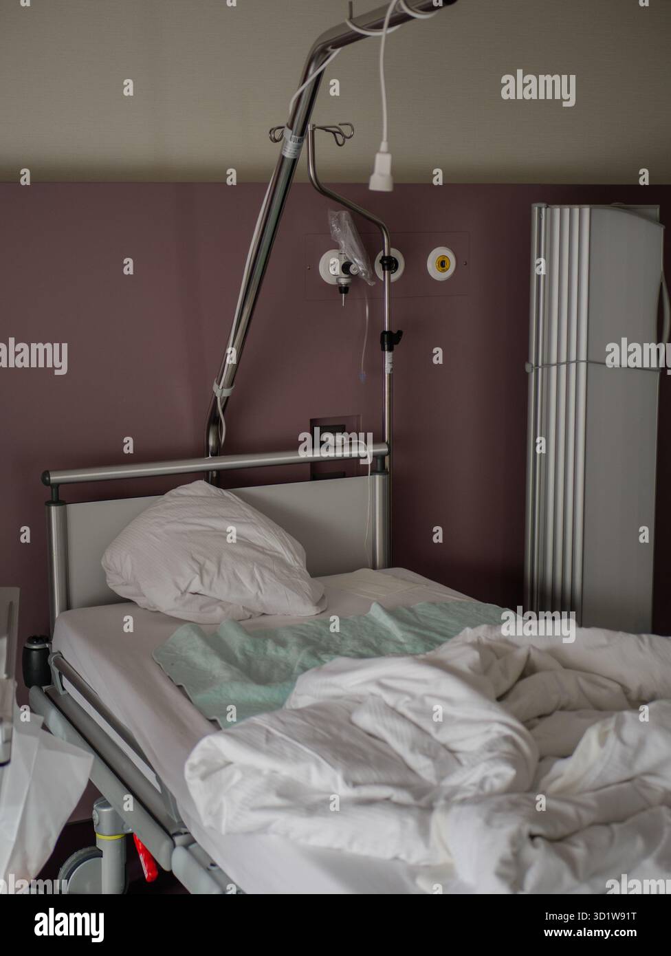 Lit d'hôpital moderne avec oreiller blanc, couverture froissée et support IV dans une chambre de patient calme. Photo de haute qualité Banque D'Images