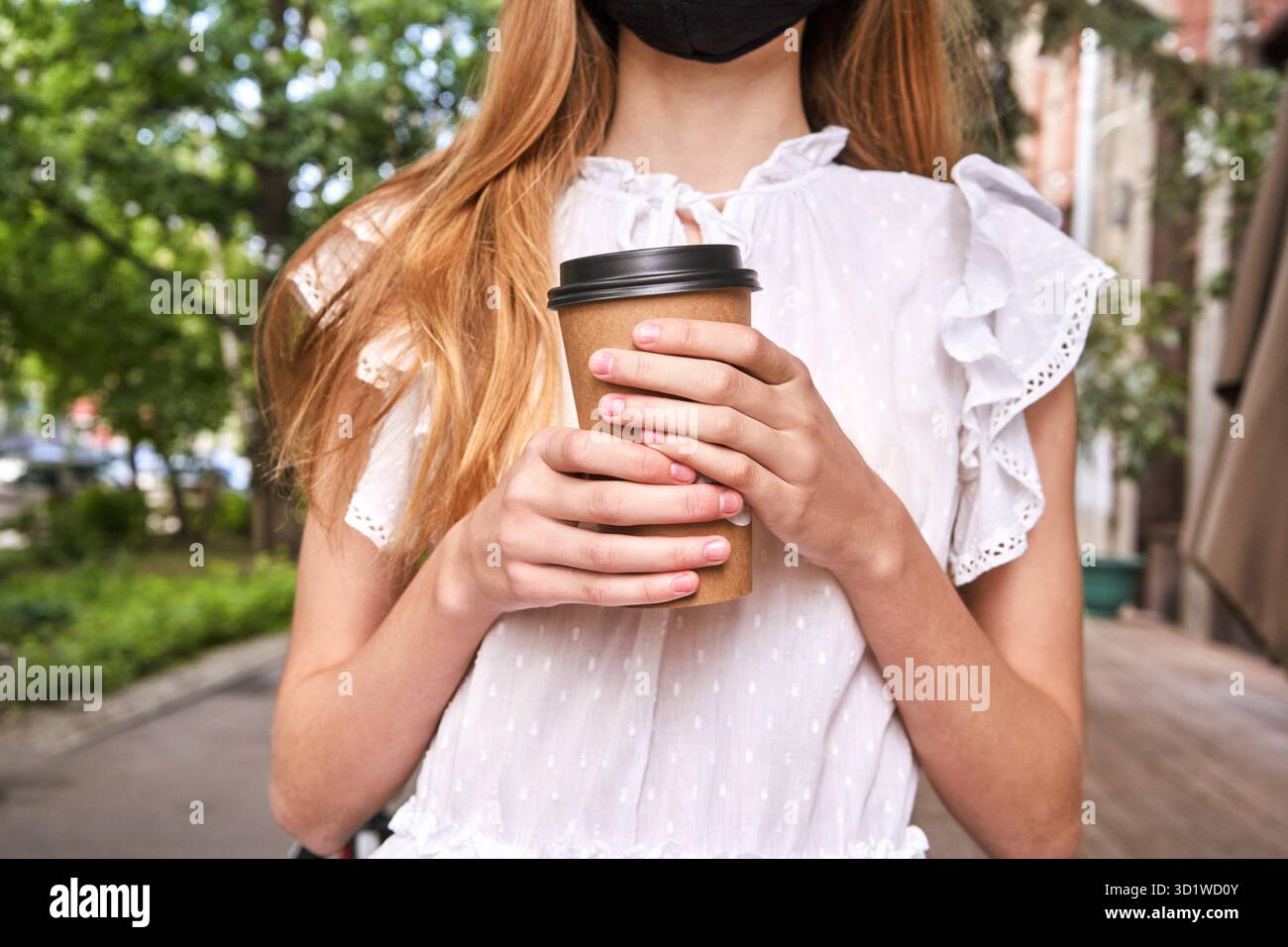 Jolie petite fille boit une boisson à l'extérieur. Achetez du café à emporter dans une tasse en plastique. Banque D'Images