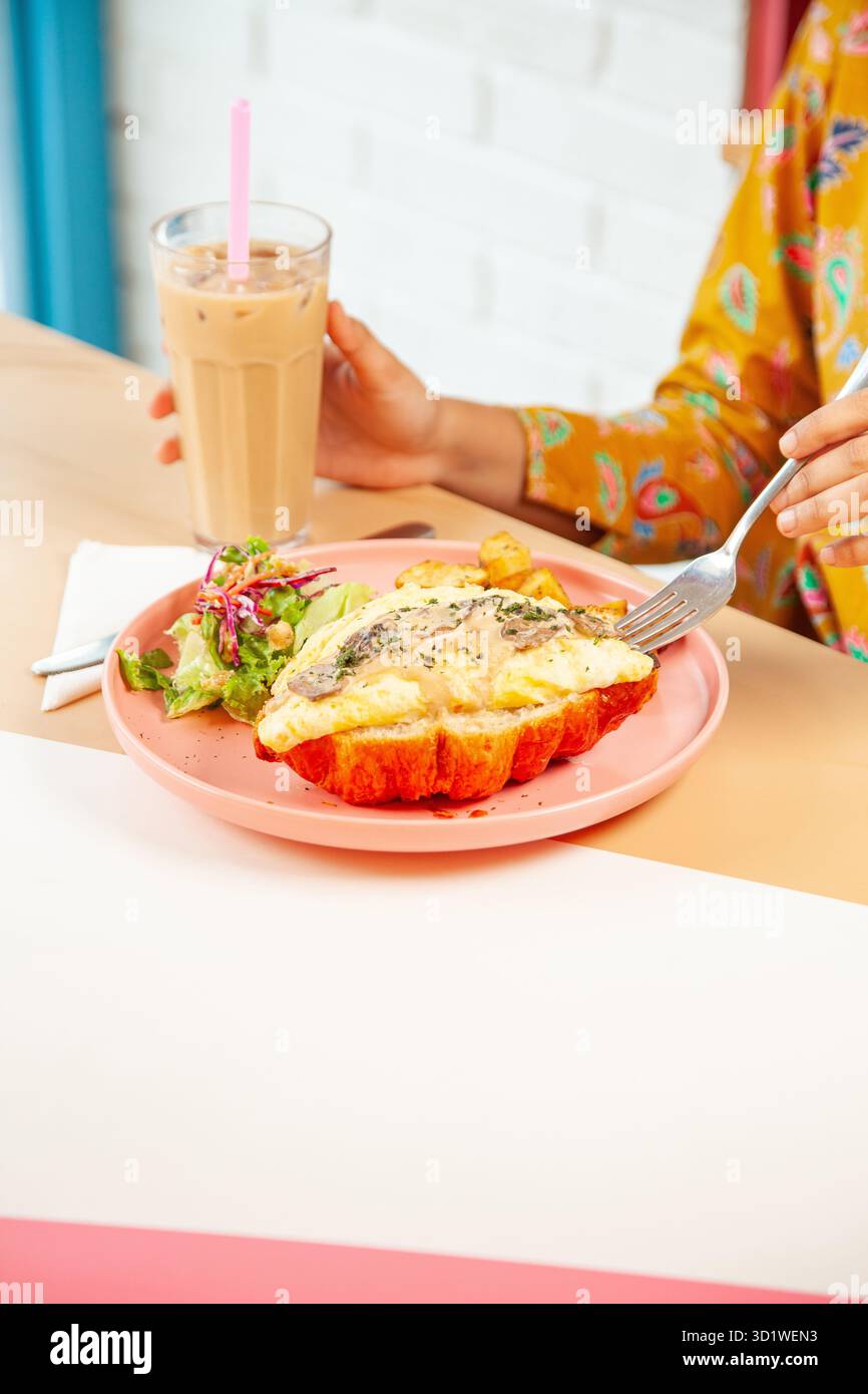 Femme appréciant le brunch petit déjeuner sandwich croissants avec café latte glacé froid. Banque D'Images