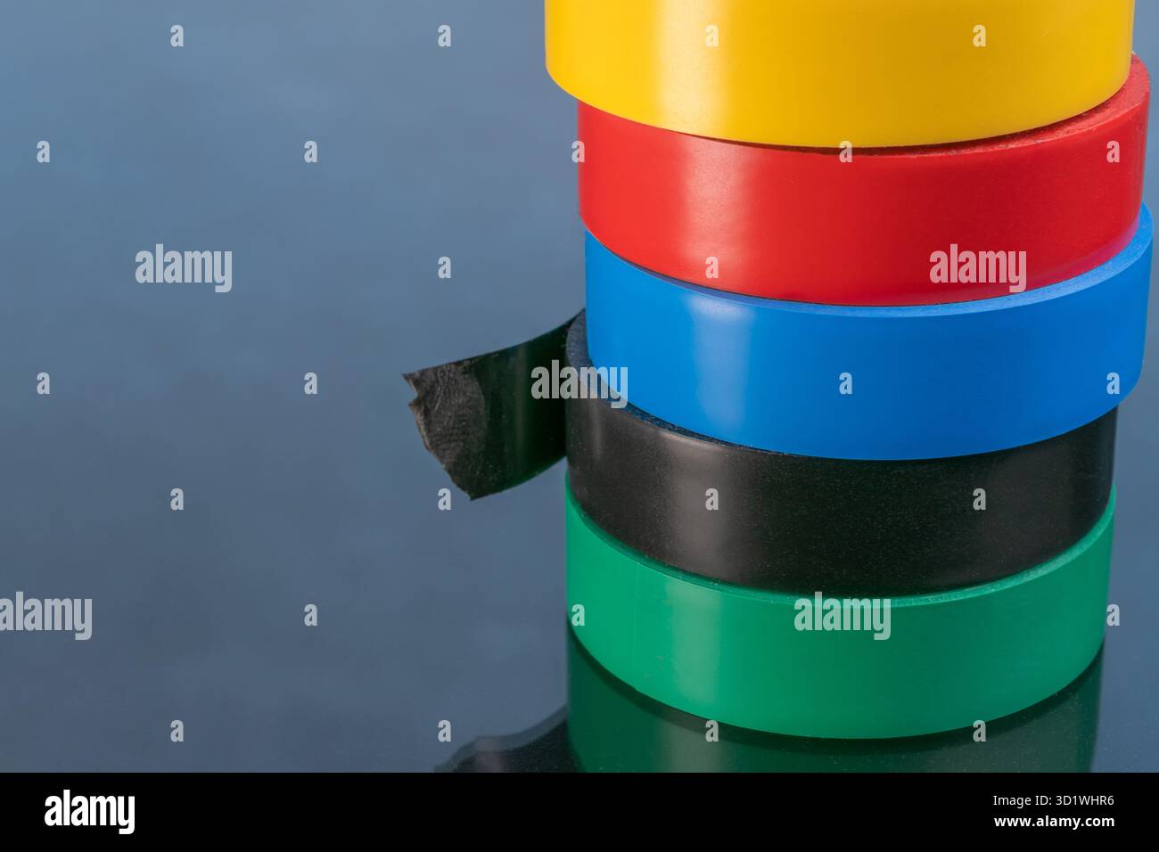 Rouleaux de ruban électrique empilés : jaune, rouge, bleu, noir, vert sur une surface réfléchissante. Banque D'Images