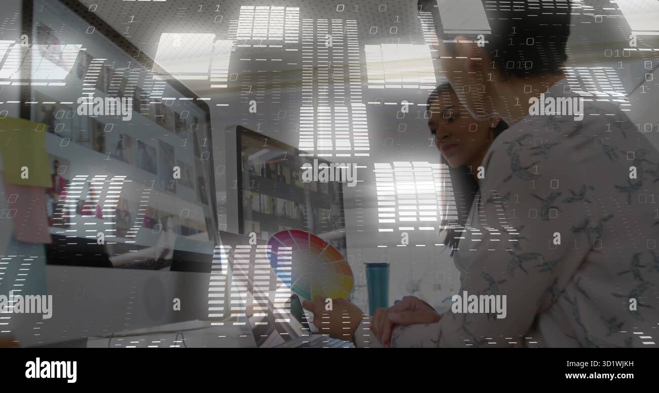 Concepteur dans la blouse florale examinant les moniteurs affichant des dessins au bureau, tenant la roue de couleur Banque D'Images