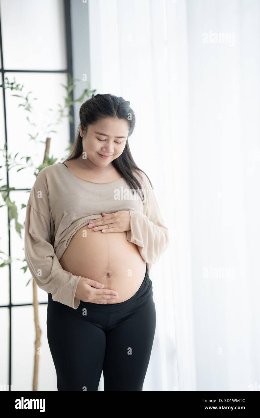 Femme asiatique enceinte tient les mains sur le ventre touchant son bébé se souciant de sa santé belle femme enceinte heureuse humeur tendre Banque D'Images