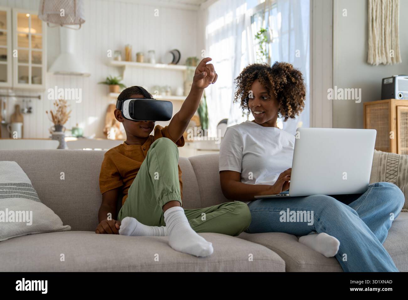 Femme afro-américaine souriante mère regardant son fils portant un simulateur de réalité virtuelle à la maison Banque D'Images