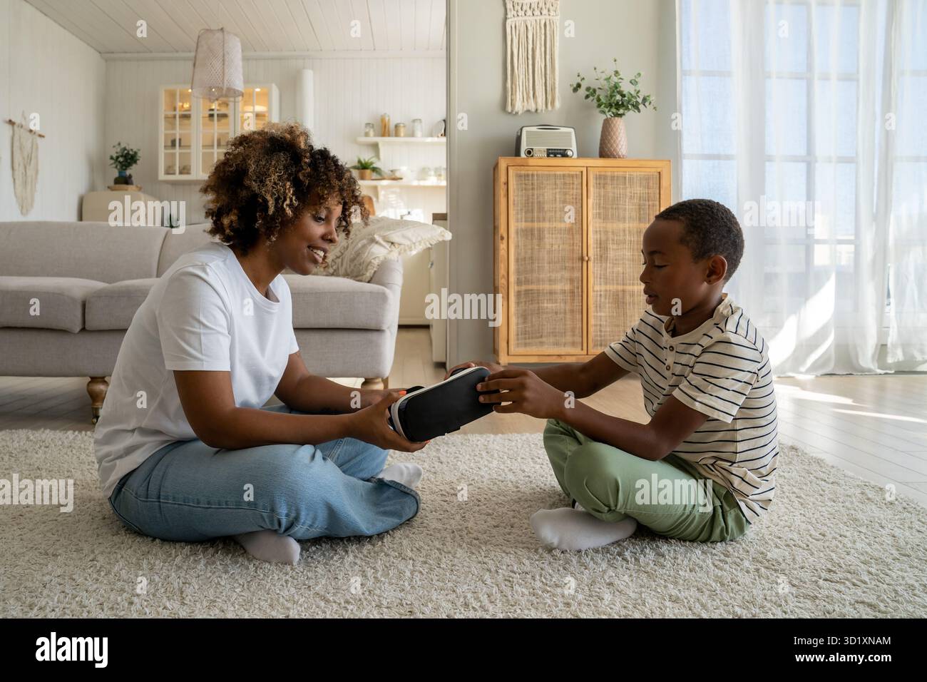 Mère et fils modernes de la famille afro-américaine assis sur le sol avec des lunettes VR Banque D'Images