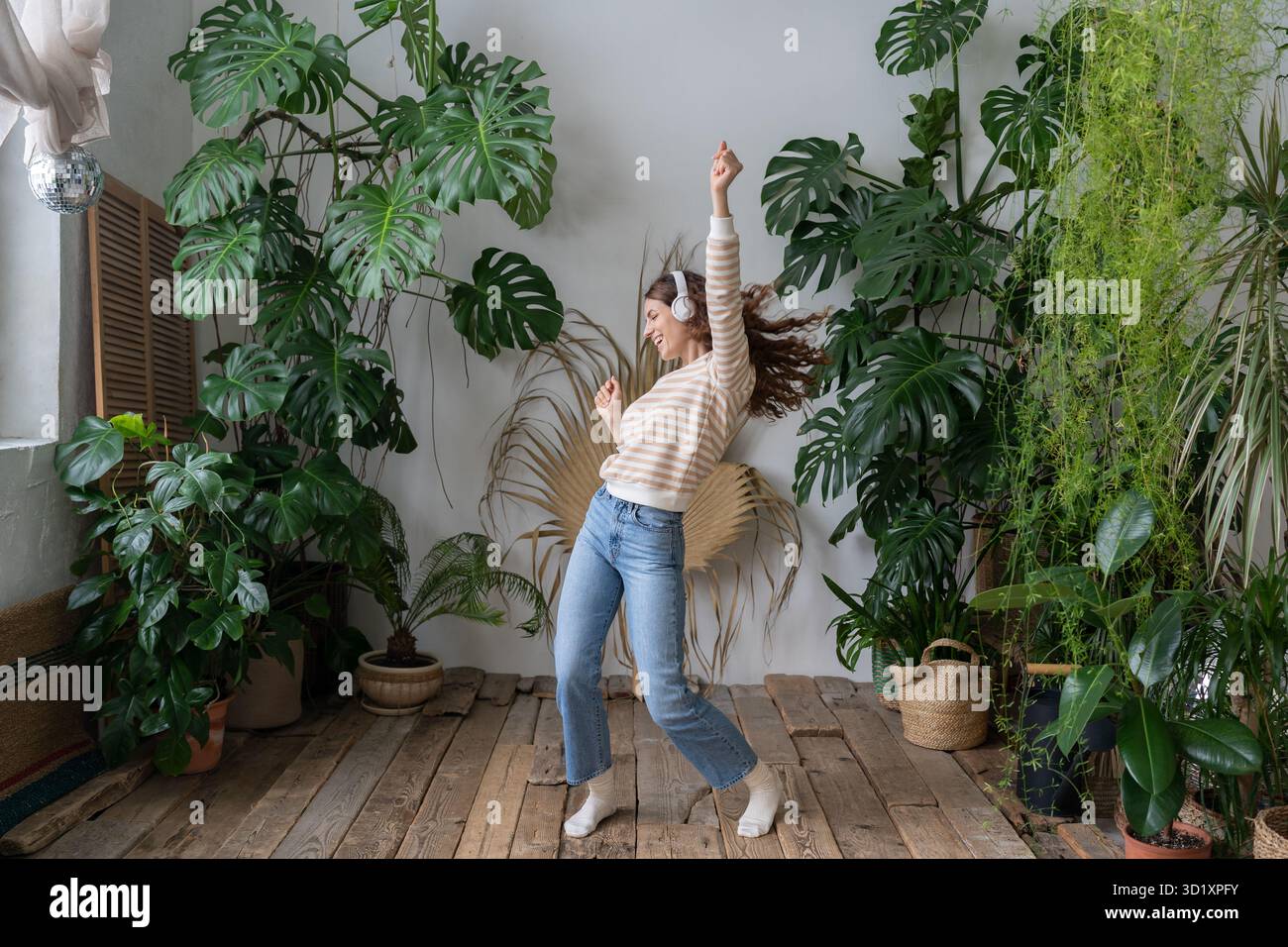 Une femme hispanique heureuse porte des écouteurs sans fil pour se détendre, dansant dans le jardin avec des plantes tropicales Banque D'Images