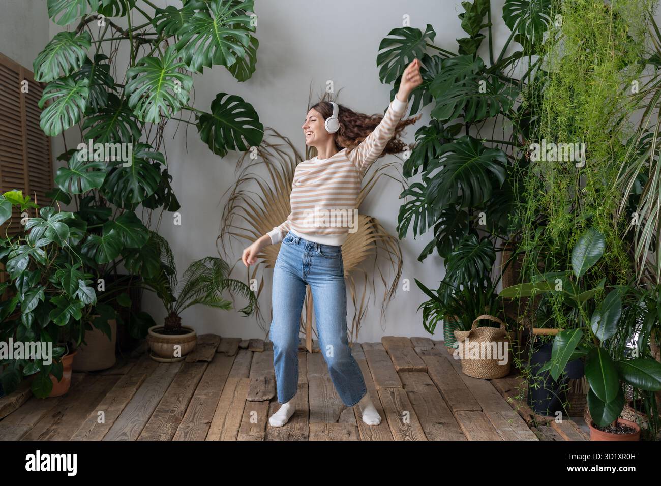 Happy Woman porte des écouteurs sans fil pour écouter de la musique, danser dans le jardin avec des plantes tropicales Banque D'Images