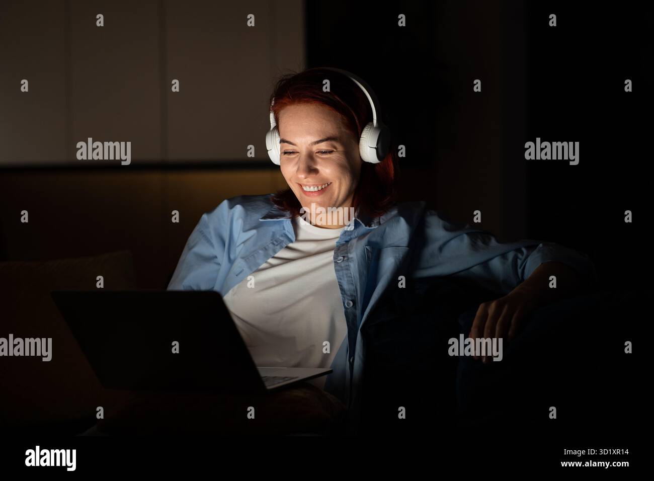 Femme insouciante détendue s'assoit confortablement avec l'ordinateur porter des écouteurs regardant un film drôle la nuit Banque D'Images