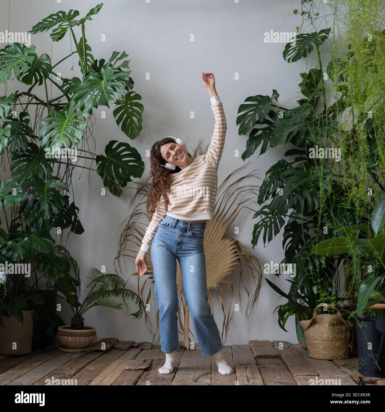 Happy Woman porte des écouteurs sans fil pour écouter de la musique, danser dans le jardin avec des plantes tropicales Banque D'Images