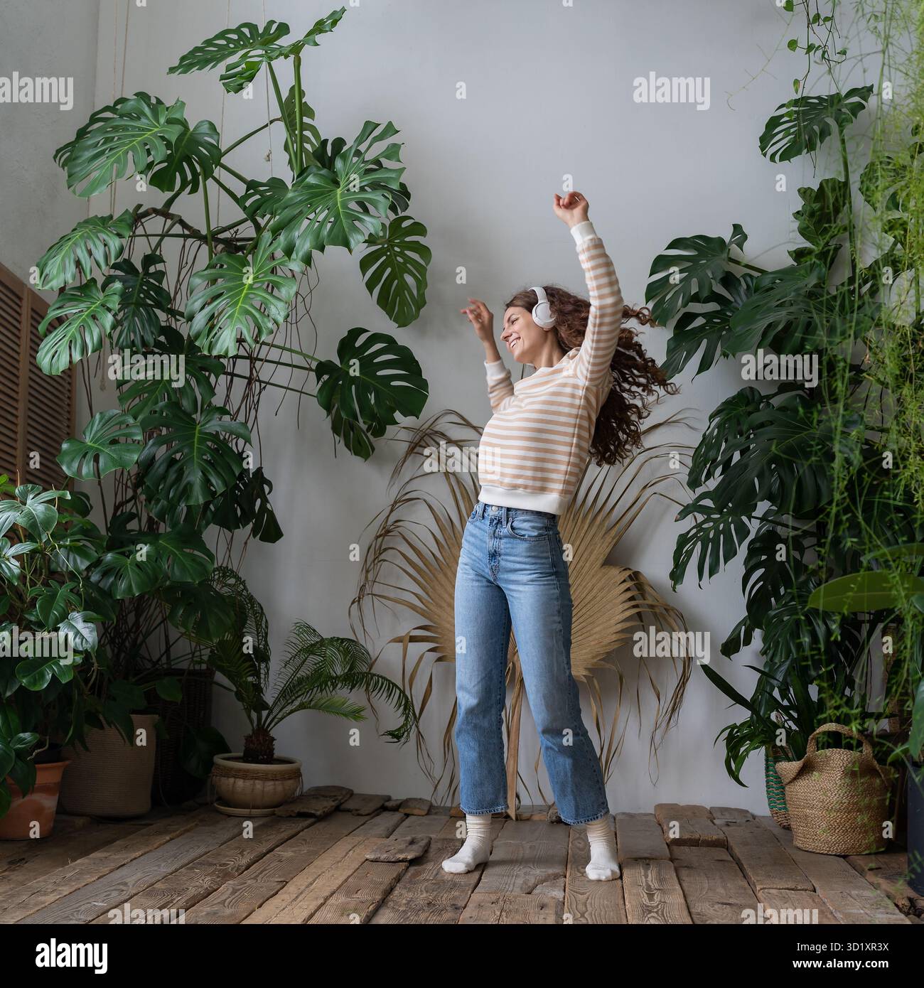 Happy Woman porte des écouteurs sans fil pour écouter de la musique, danser dans le jardin avec des plantes tropicales Banque D'Images