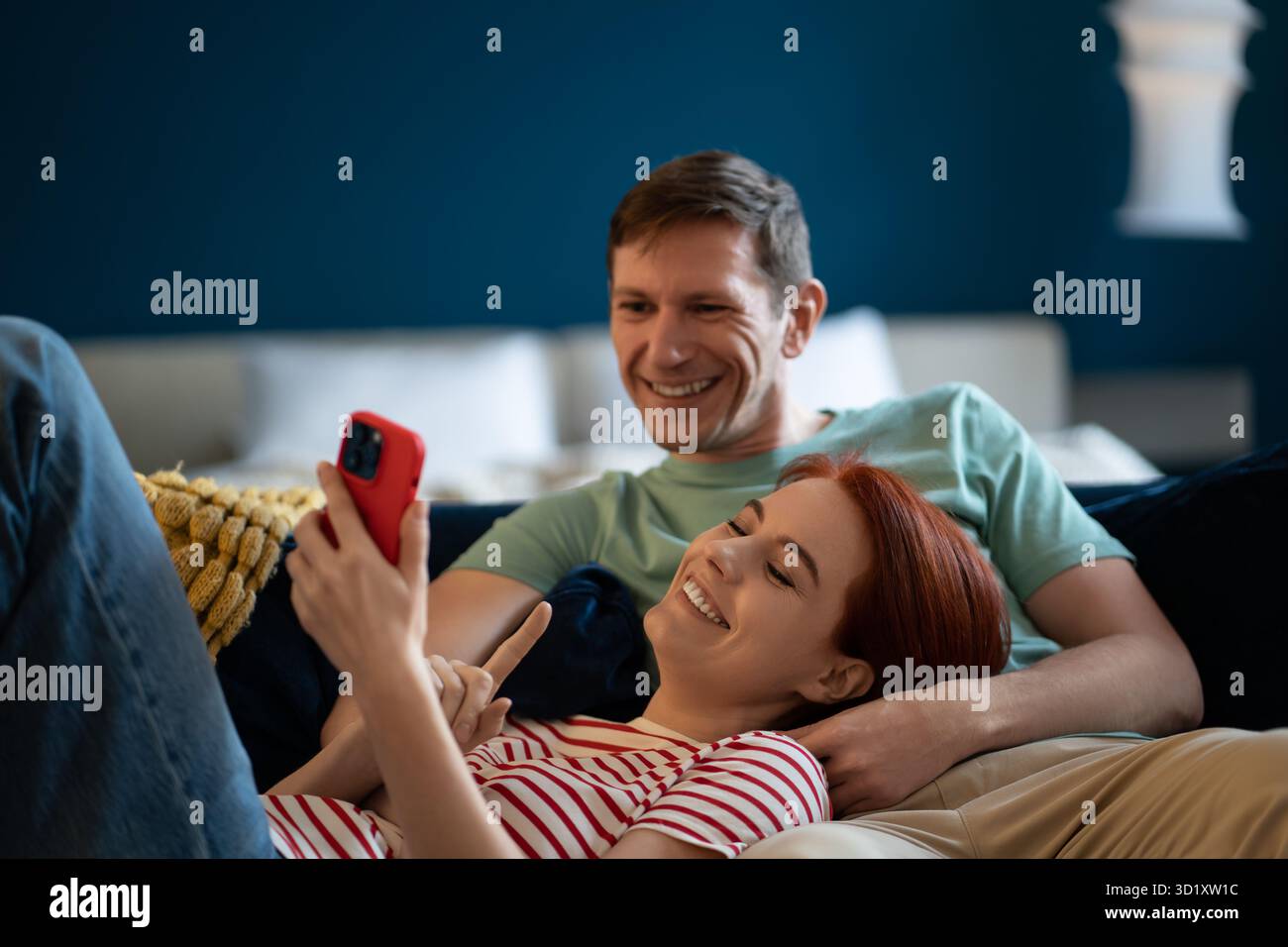 Heureux souriant homme et femme couché détendu sur le canapé look écran téléphone. Achats en ligne en famille positifs Banque D'Images