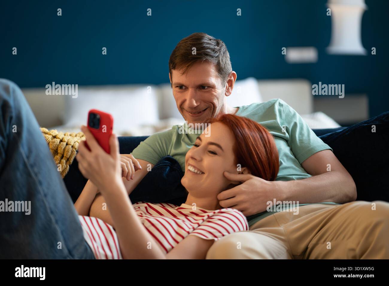 Heureux souriant homme et femme couché détendu sur le canapé look écran téléphone. Achats en ligne en famille positifs Banque D'Images