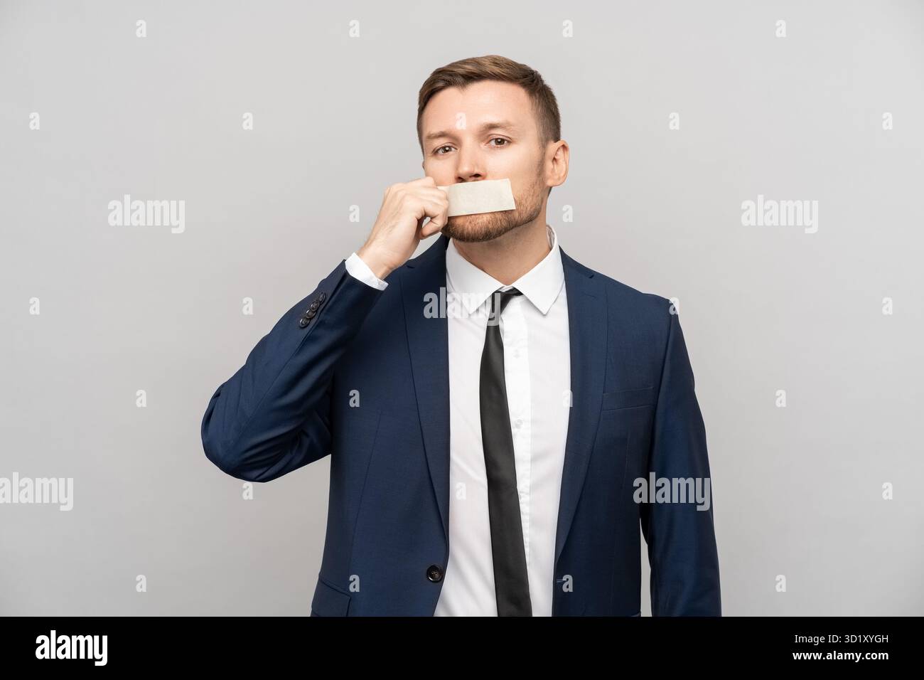Homme d'affaires en costume formel épluche la bande de ruban adhésif des lèvres comme signe de la liberté d'expression de la parole Banque D'Images