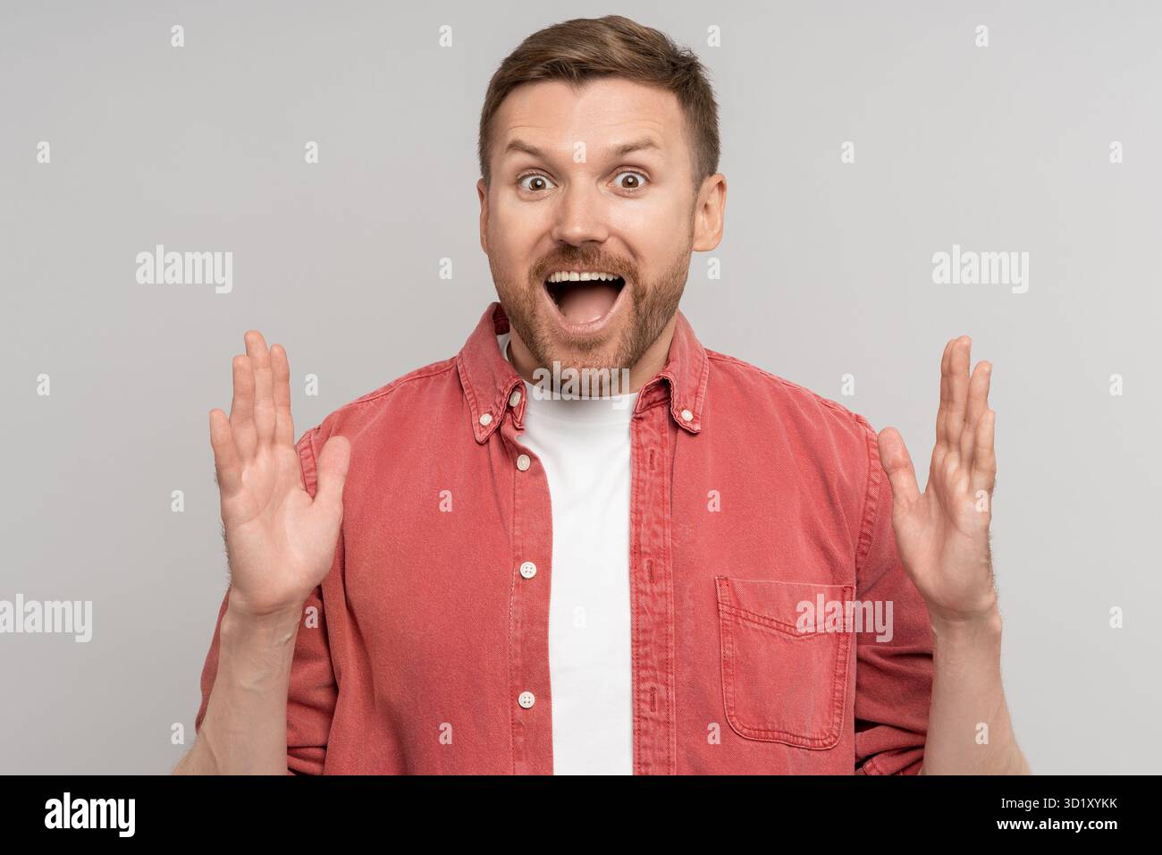 Homme souriant surpris avec la bouche ouverte écartant les mains paumes vers le haut regarder la caméra au-dessus de l'arrière-plan du studio Banque D'Images