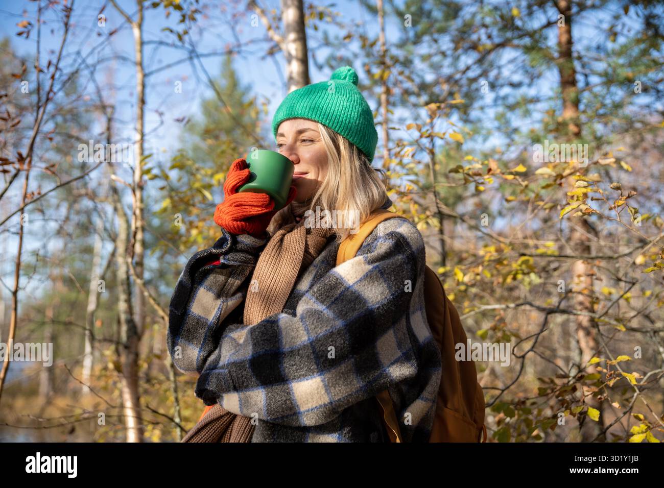 Joyeuse femme agréablement souriante appréciant boire du thé chaud tout en passant un passe-temps dans la nature sauvage Banque D'Images