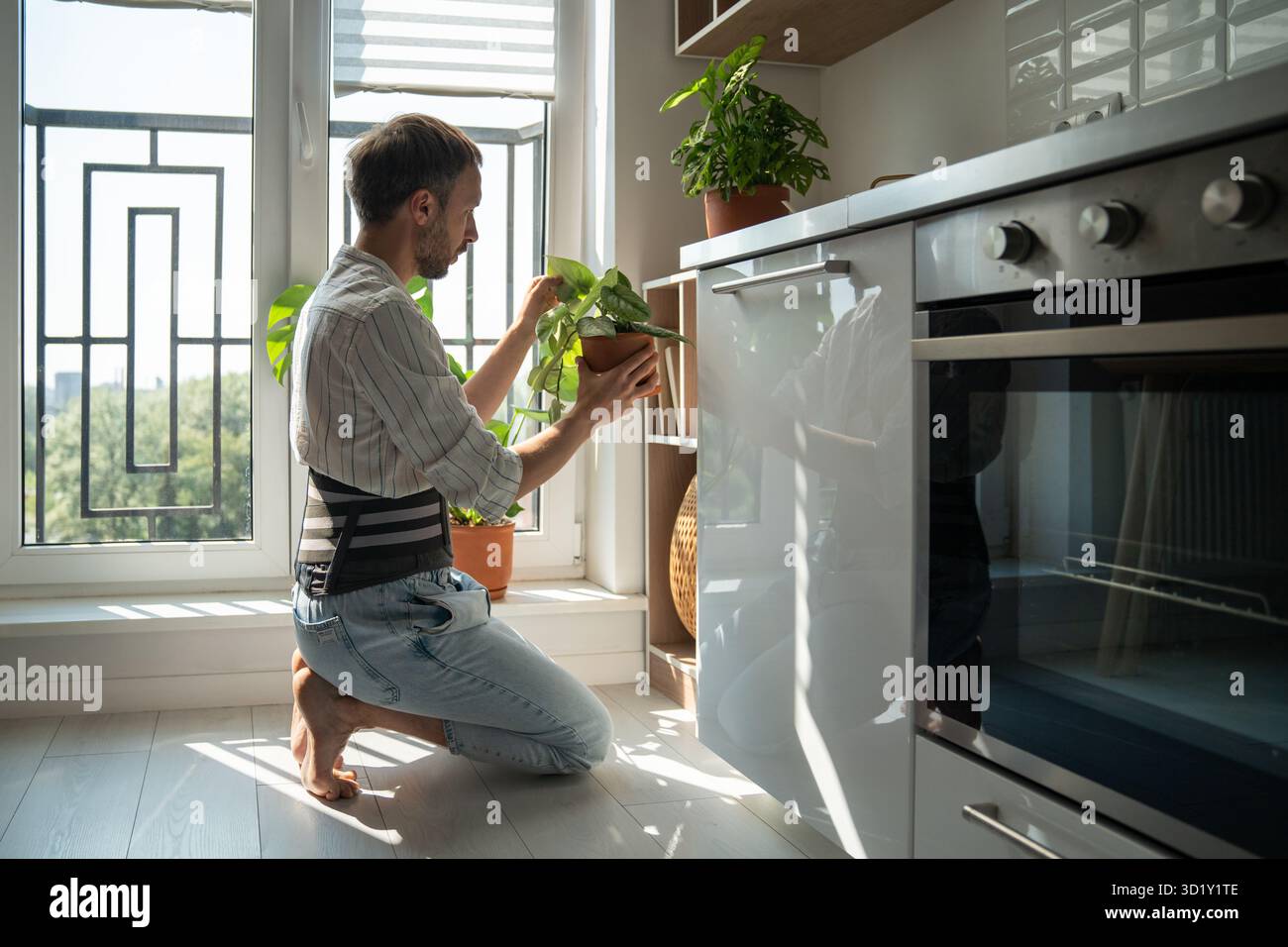 Jeune homme portant une ceinture de soutien dorsal prenant soin des plantes d'intérieur à la maison Banque D'Images