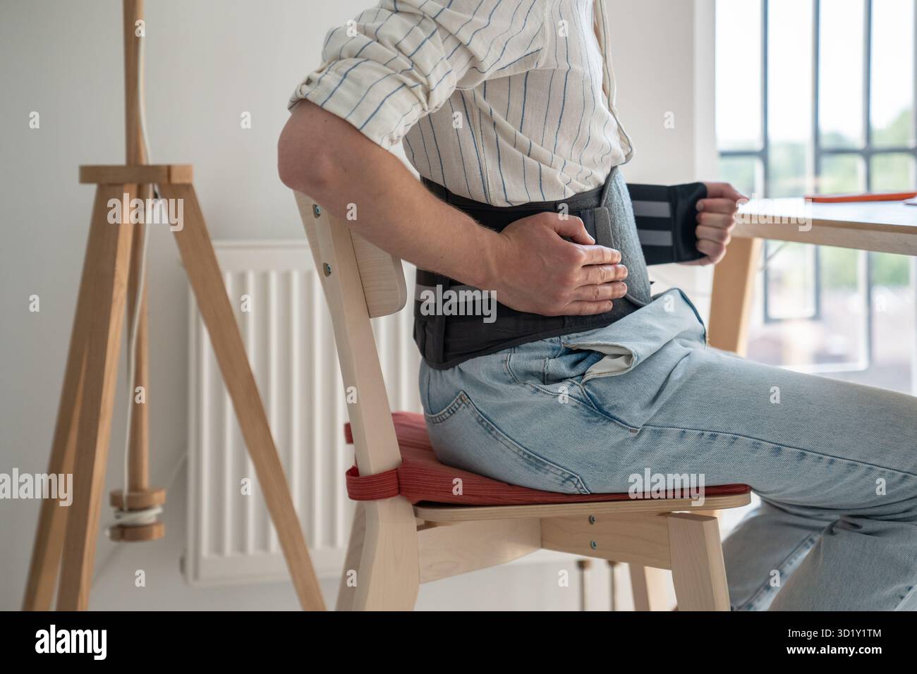 Homme assis à table portant un corset médical pour rachis lombaire Banque D'Images