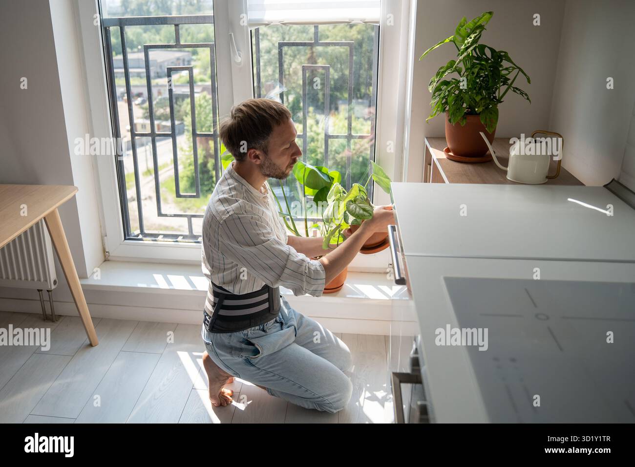 Jeune homme portant une ceinture de soutien dorsal prenant soin des plantes d'intérieur à la maison Banque D'Images