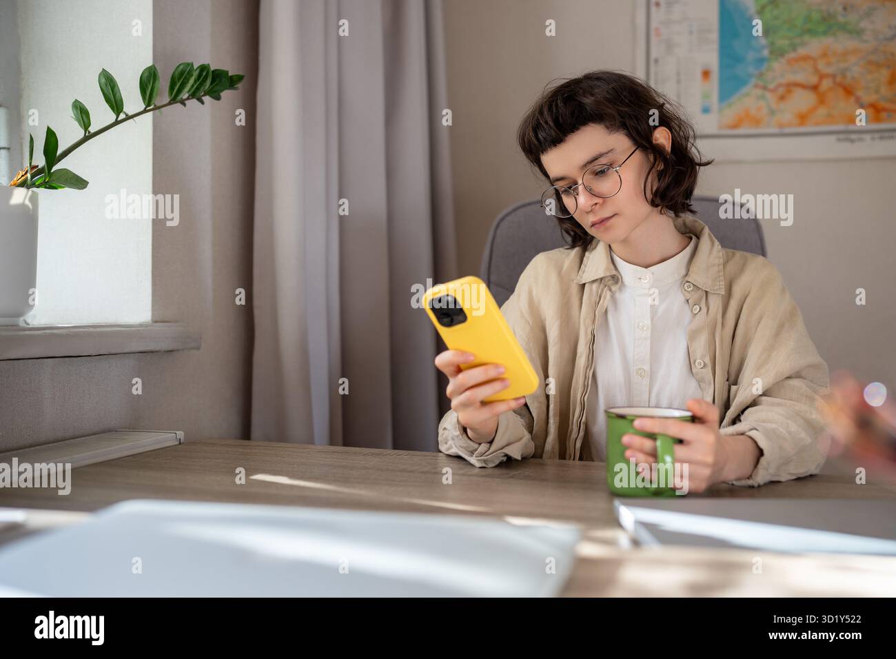 Étudiant fille fatigué parcourant les médias sociaux dans smartphone assis au bureau après l'étude prendre une pause avec le thé Banque D'Images