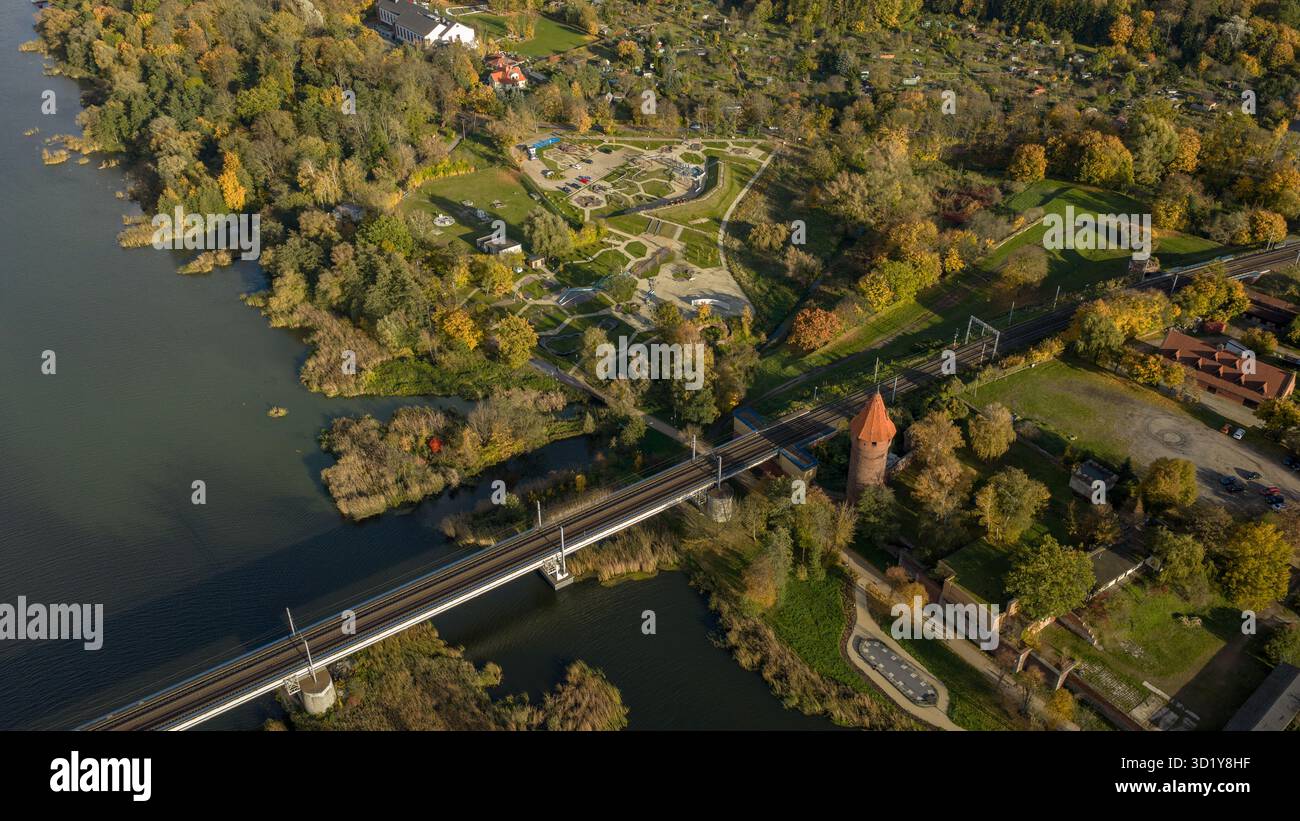La vue aérienne montre le parc du château de Malbork à Malbork, en Pologne, avec la rivière Nogat à gauche, un pont de chemin de fer menant à l'enceinte, une tour conique, des murs et un patt Banque D'Images