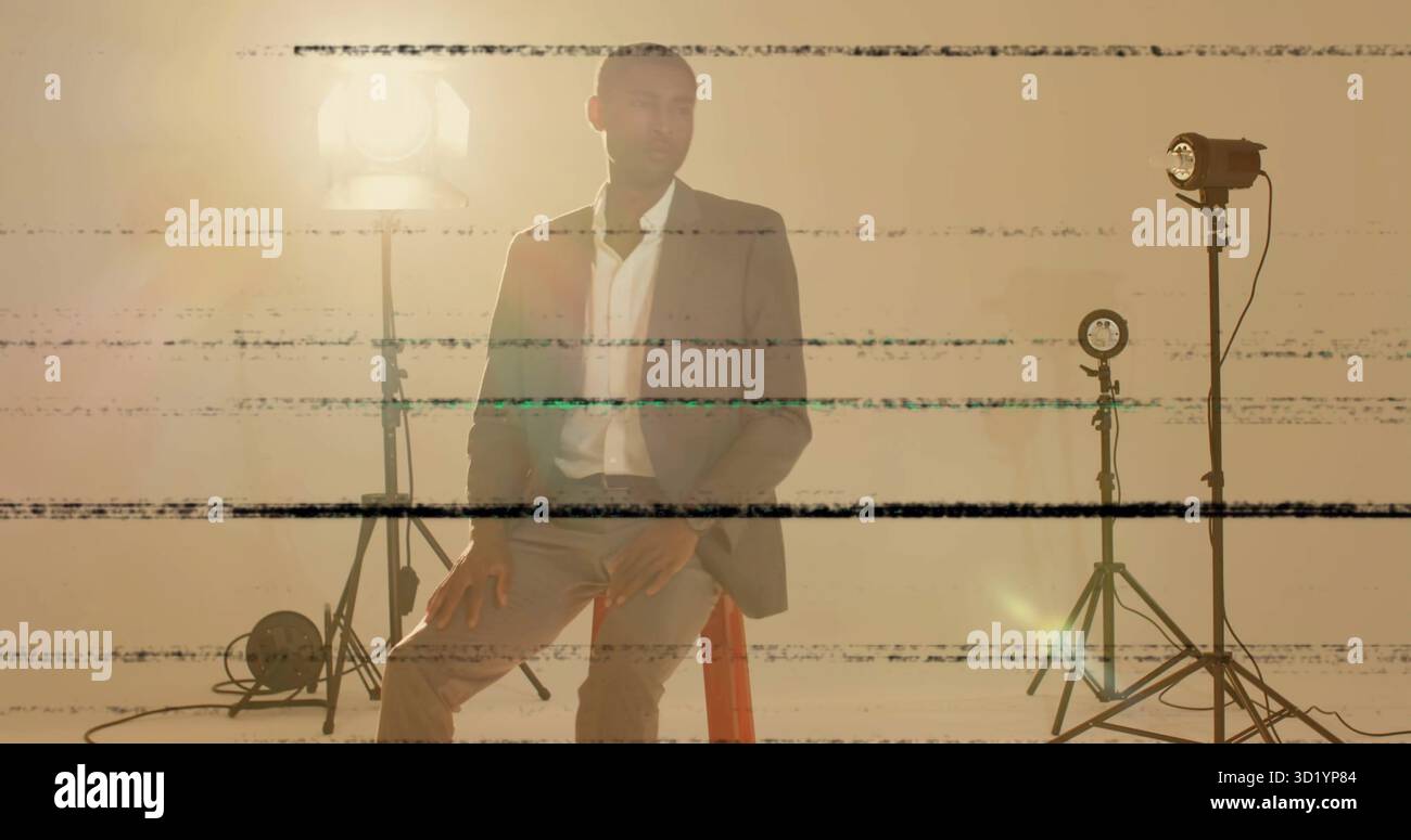 Homme noir assis sur le tabouret portant une tenue d'affaires dans le studio, avec des lumières, des câbles, des lignes de pépins Banque D'Images