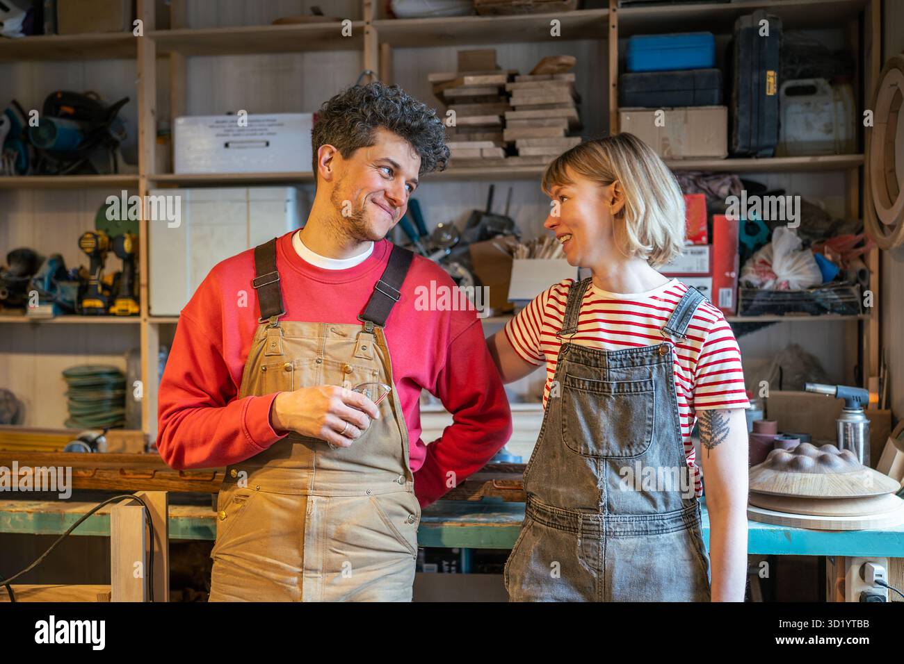 Couple de charpentier souriant bavardant et flirtant lors de la pause dans l'atelier de bois. Affaire familiale, lien romantique Banque D'Images
