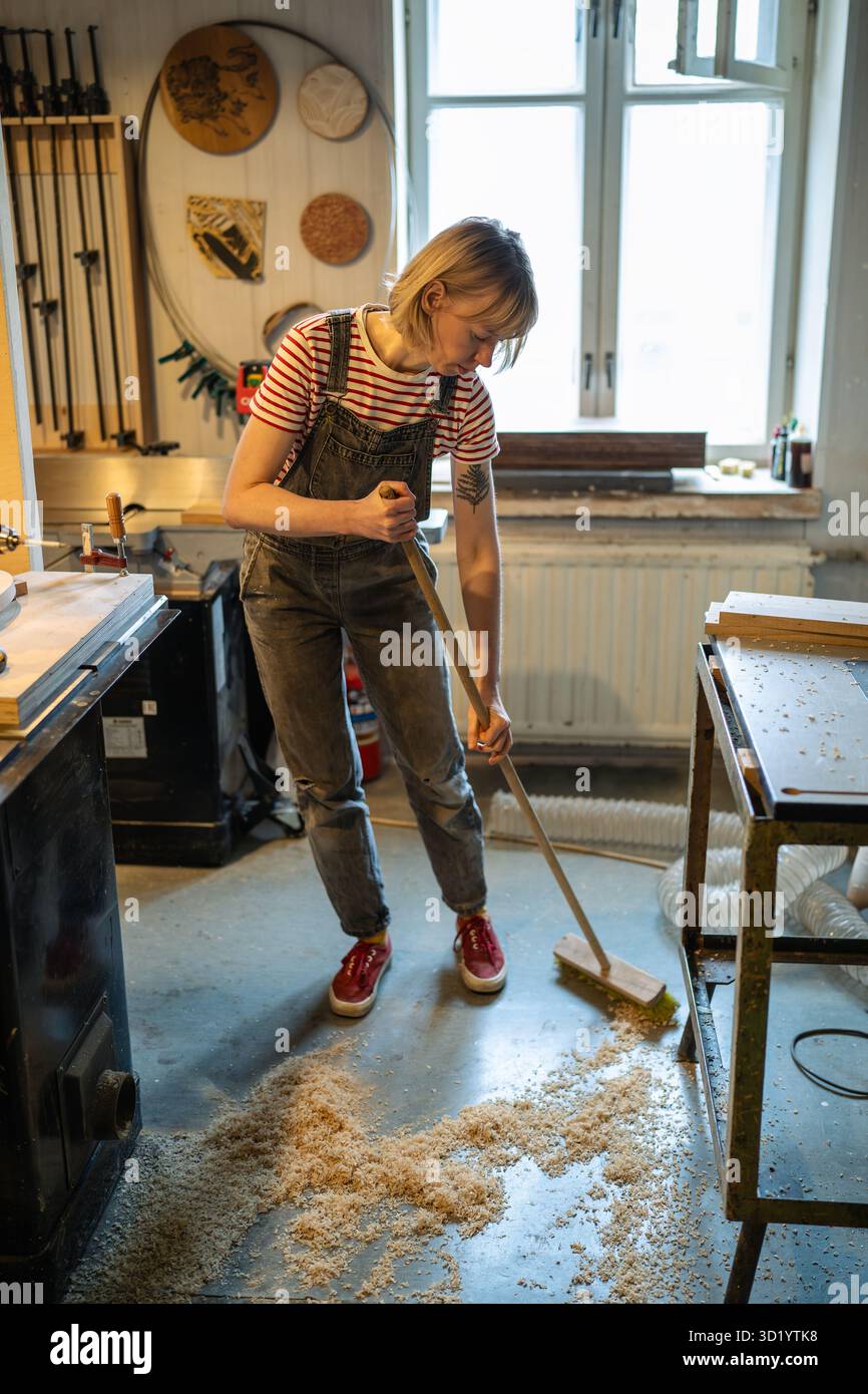 Femme charpentier nettoyant l'atelier après le travail. Handywoman balayer la sciure de bois et ventiler pour la santé Banque D'Images