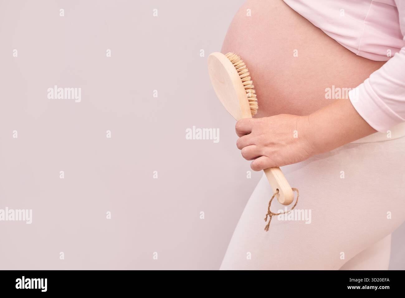 Femme caucasienne enceinte exfoliant le ventre avec une brosse corporelle pour la routine de soins de la peau Banque D'Images
