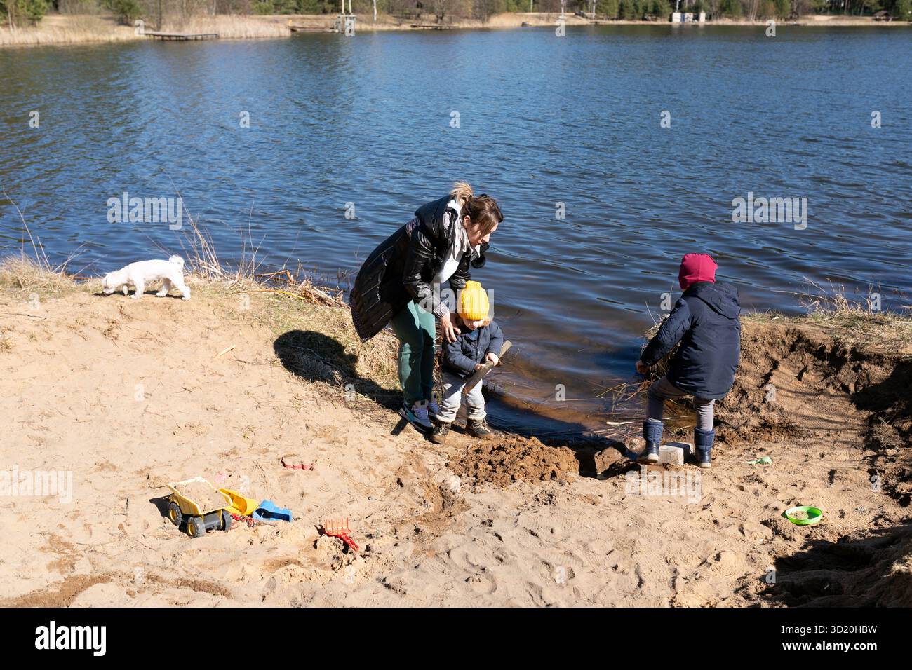 Les enfants jouent dans le sable au bord du lac avec un adulte surveillant un jour ensoleillé de printemps Banque D'Images