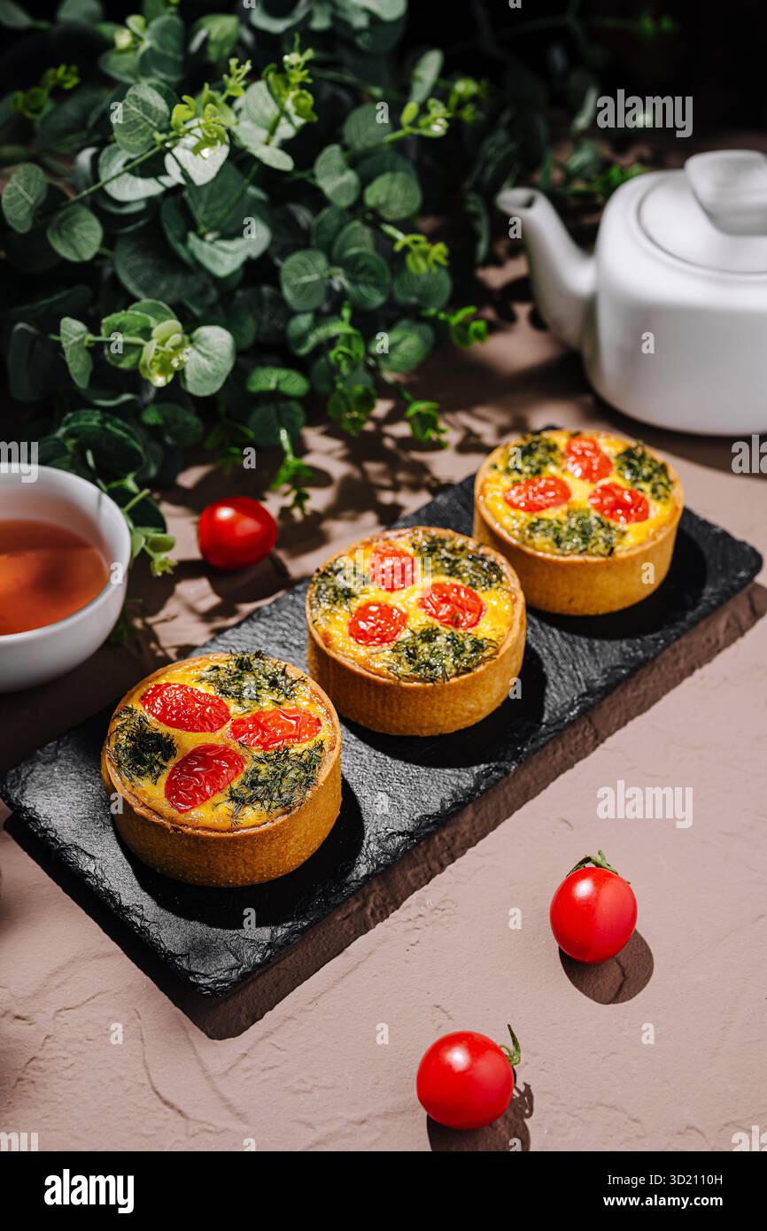 Tartes salées colorées aux épinards et tomates cerises servies sur une assiette en ardoise avec du thé Banque D'Images