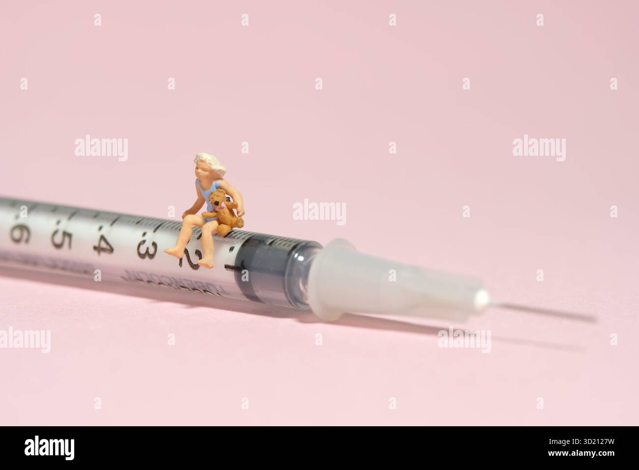 Photographie miniature de figurine de jouet de personnes minuscules. Une petite fille assise au-dessus de la seringue aiguille tenant la poupée ours en peluche. Isolé sur fond rose. Image Banque D'Images