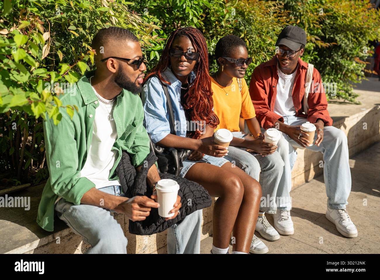 Groupe animé d'amis d'université afro-américains appréciant la conversation avec des boissons à emporter dans le parc Banque D'Images