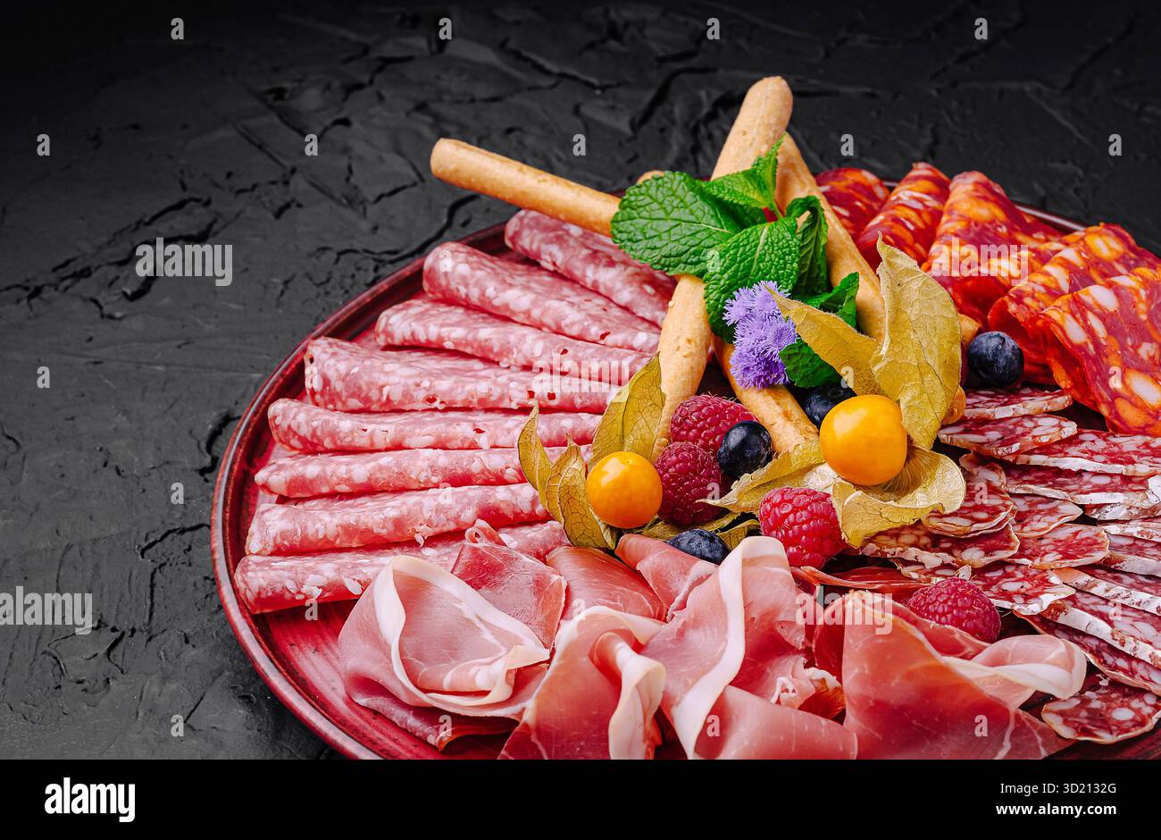 Viandes et fruits salés disposés magnifiquement sur un plateau sombre pour une présentation gourmande Banque D'Images