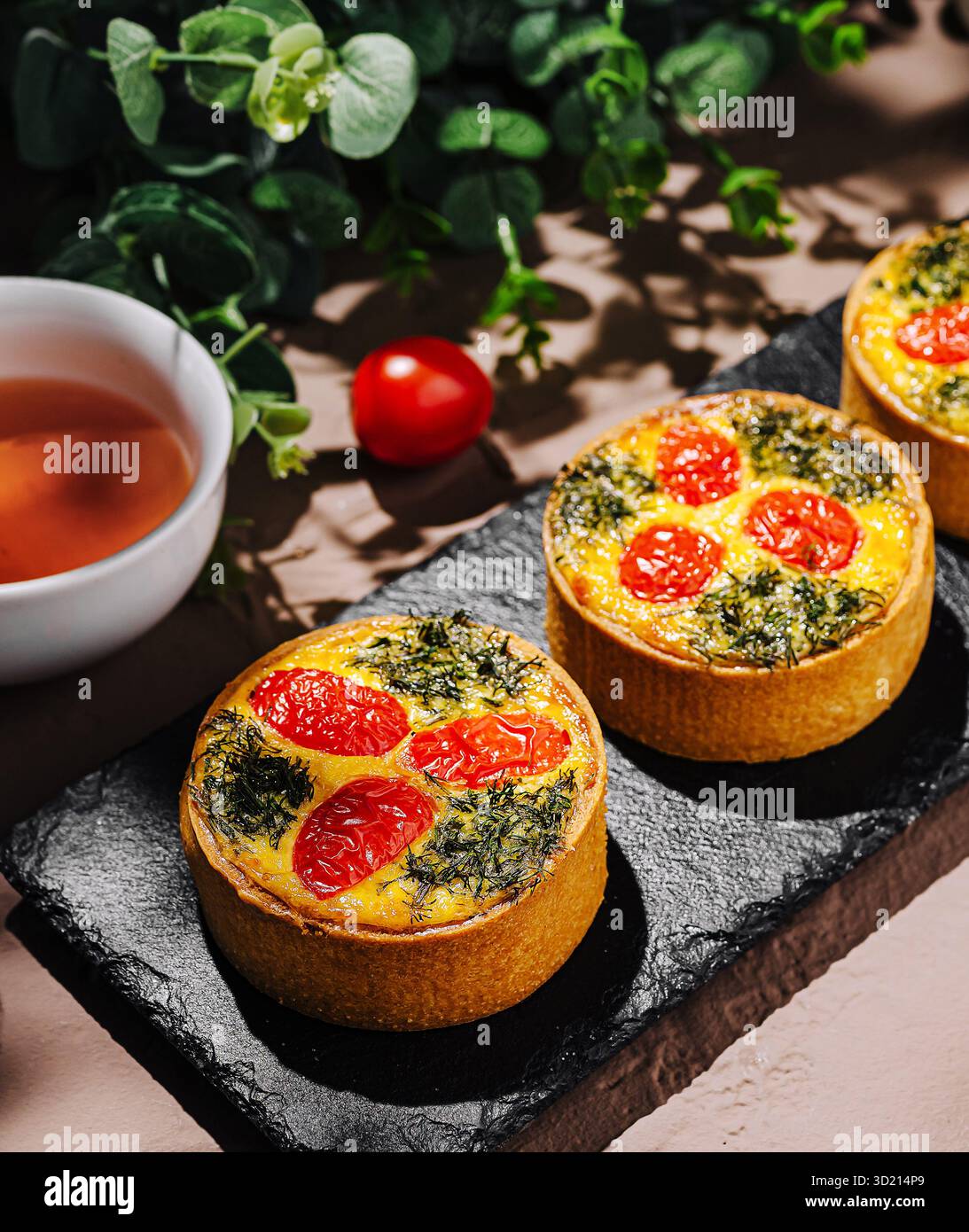 Tartes salées avec tomates et herbes sur une planche de service en ardoise Banque D'Images